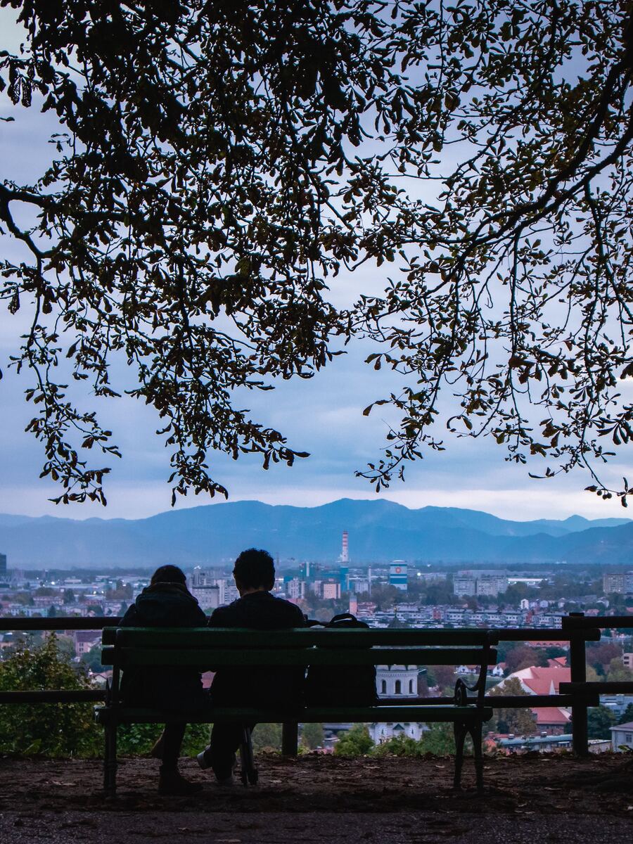 Two people on a bench above Ljubljana, looking out over the city at dusk